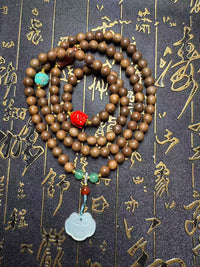Tibetan wooden prayer beads necklace with jade pendant and colorful spacer beads on calligraphy background