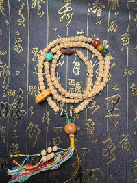 Natural wood Buddhist prayer beads mala with colorful tassel and decorative accents on calligraphy background