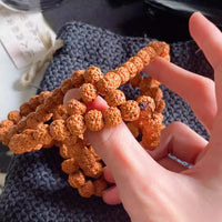 Hand holding natural rudraksha prayer beads with textured seeds