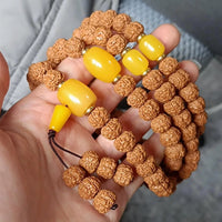 Hand holding Rudraksha mala beads with large yellow amber spacers for meditation and prayer