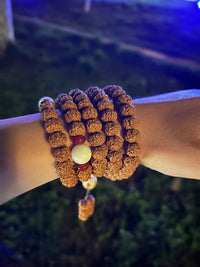 Rudraksha prayer beads bracelet wrapped on wrist with white and red accent beads, outdoor night background