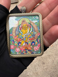Hand holding Tibetan Buddhist amulet pendant with colorful thangka painting in ornate metal frame