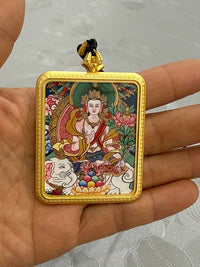 Hand holding a Buddhist pendant with golden frame and colorful deity painting