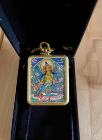 Colorful Buddhist pendant with deity painting in gold frame, placed inside black jewelry box