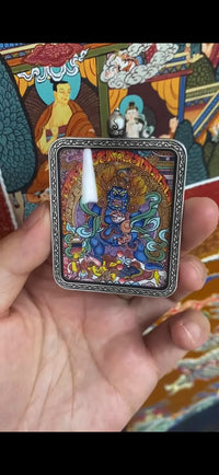 Tibetan thangka amulet pendant with wrathful deity artwork, held in hand against colorful background