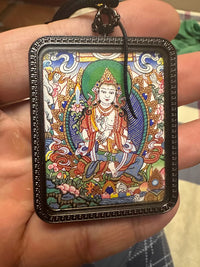 Hand holding Tibetan thangka pendant with colorful Buddha painting in black frame, Buddhist necklace jewelry