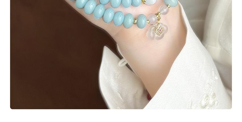 Handheld close view of the translucent flower pendant with water-blue and pale beads against a white sleeve.
