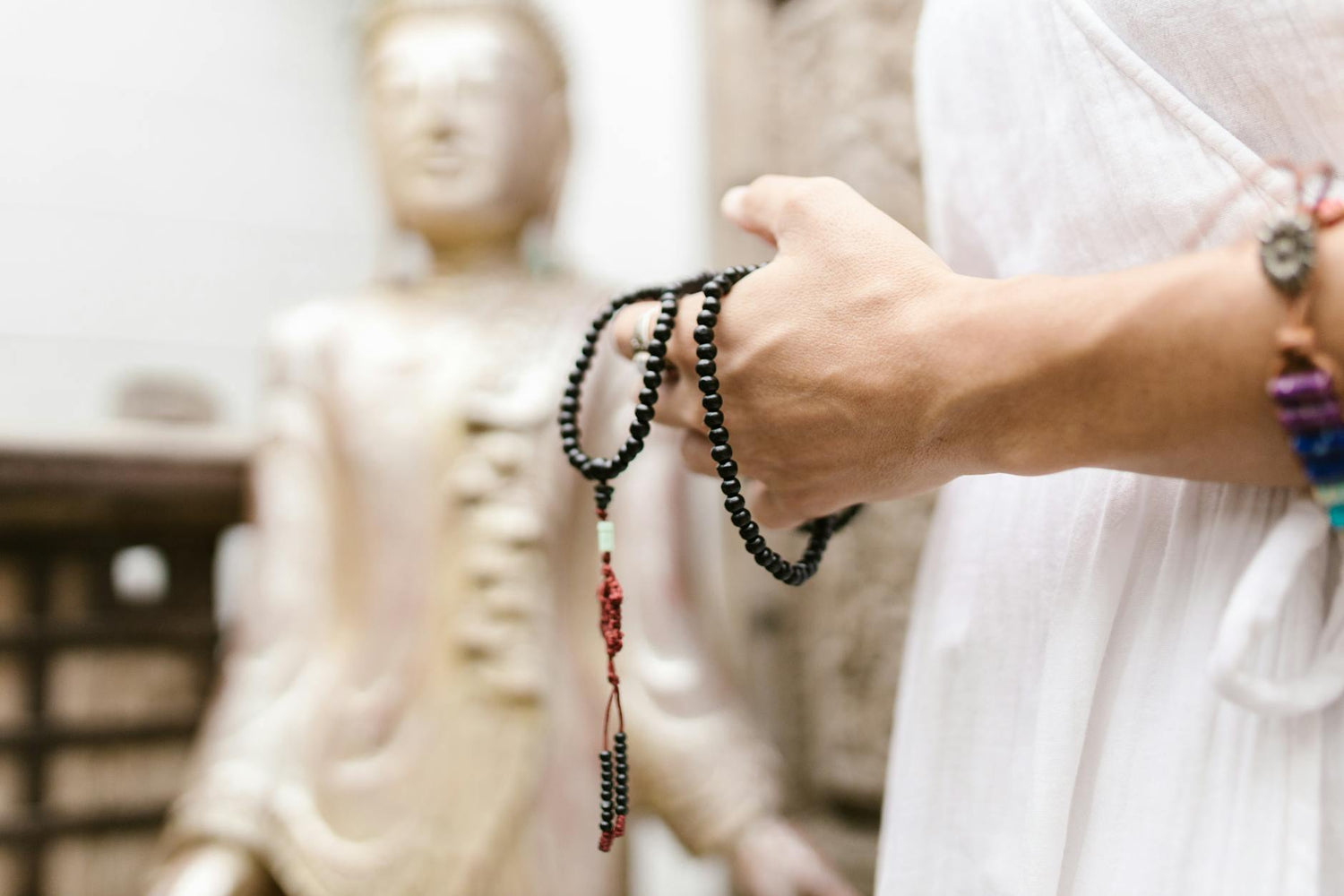 taoist prayer beads vs buddhist mala - A close-up of a hand holding black prayer beads near a blurred Buddha statue, symboli…