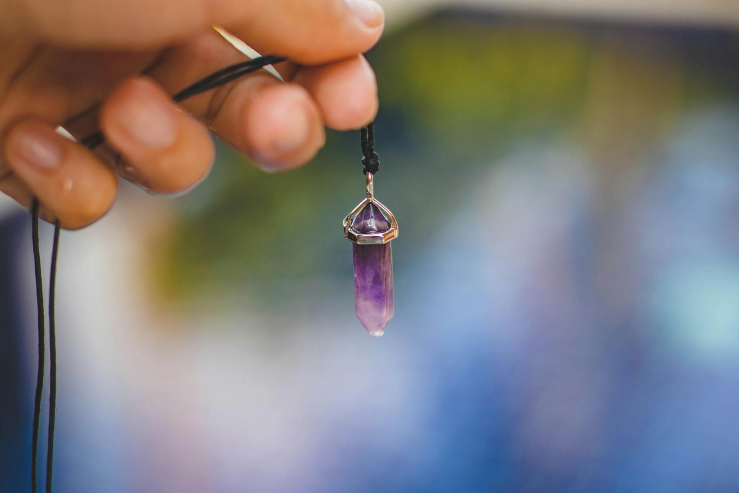 taoist healing jewelry - Close-up of a hand holding a purple amethyst pendant against a blurred outdoor background. | Buddha…
