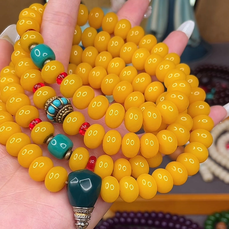 Hand holding 108 yellow amber mala beads with turquoise and coral accents, Tibetan Buddhist prayer beads for meditation and blessings