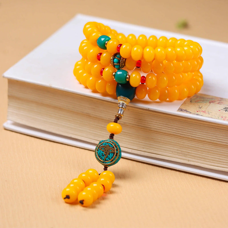 108 yellow amber mala beads with turquoise and coral accents wrapped around a book, Tibetan Buddhist prayer beads for meditation and protection