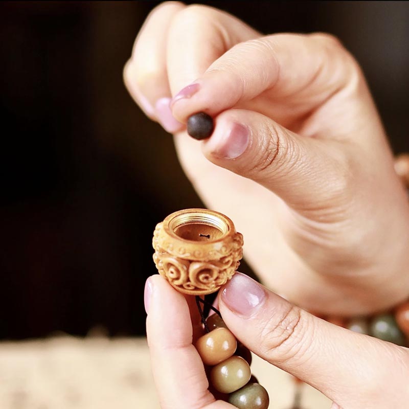 Close-up of hands inserting bead into Tibetan mala guru bead, handmade meditation prayer necklace detail