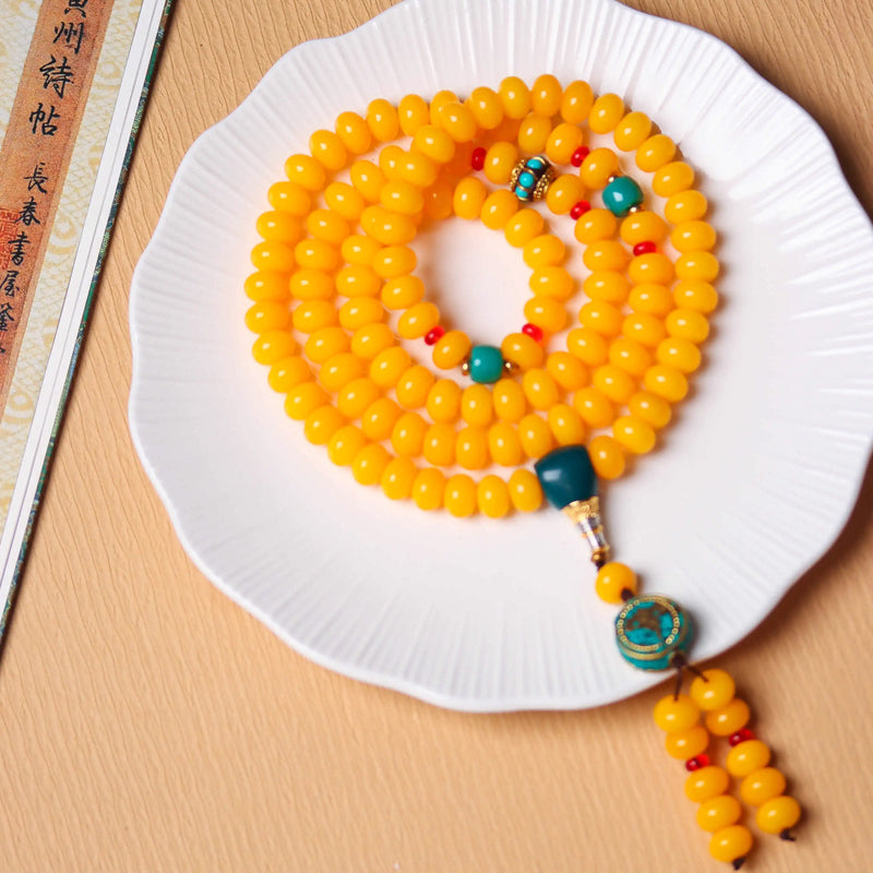 108 yellow amber mala beads with turquoise and coral accents displayed on a white plate for Tibetan Buddhist meditation