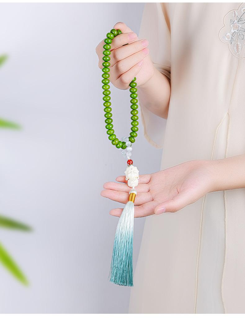 Green bodhi-root strand held in one hand, showing its pale figurine and full blue-green tassel.