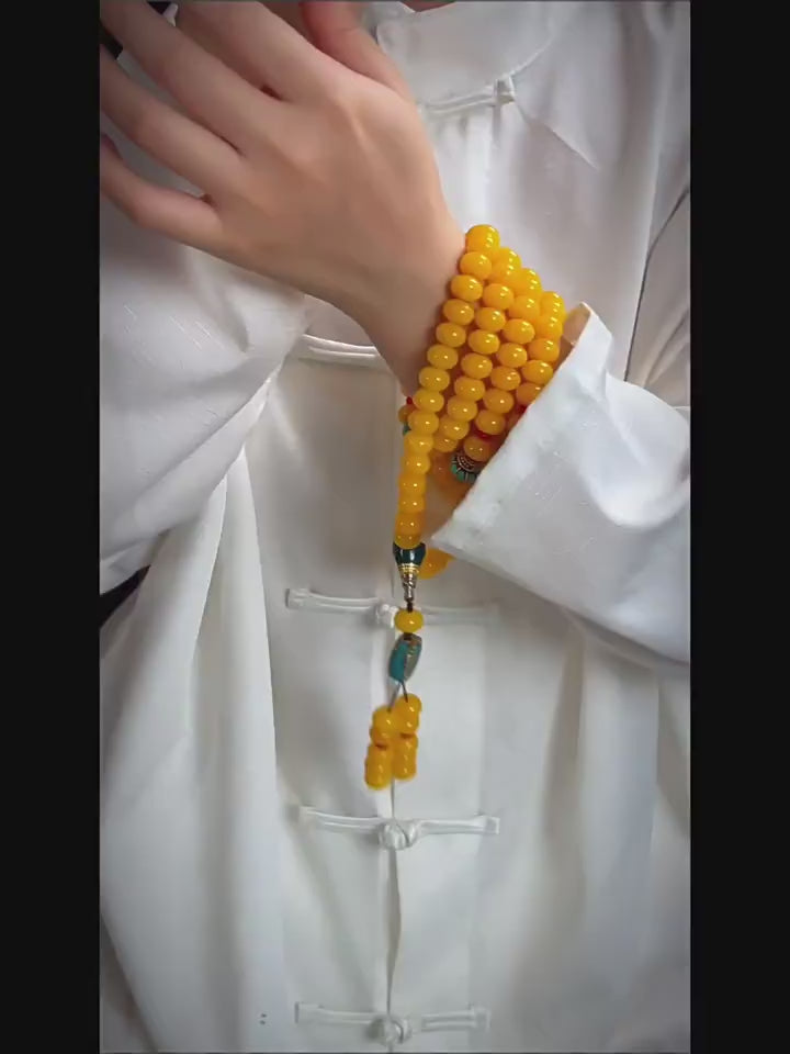 Person wearing 108 yellow amber mala beads with turquoise and coral accents, Tibetan Buddhist prayer beads for meditation and blessings