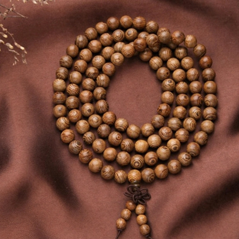 Striped wood mala coiled on fabric, showing round beads and two short beaded tails